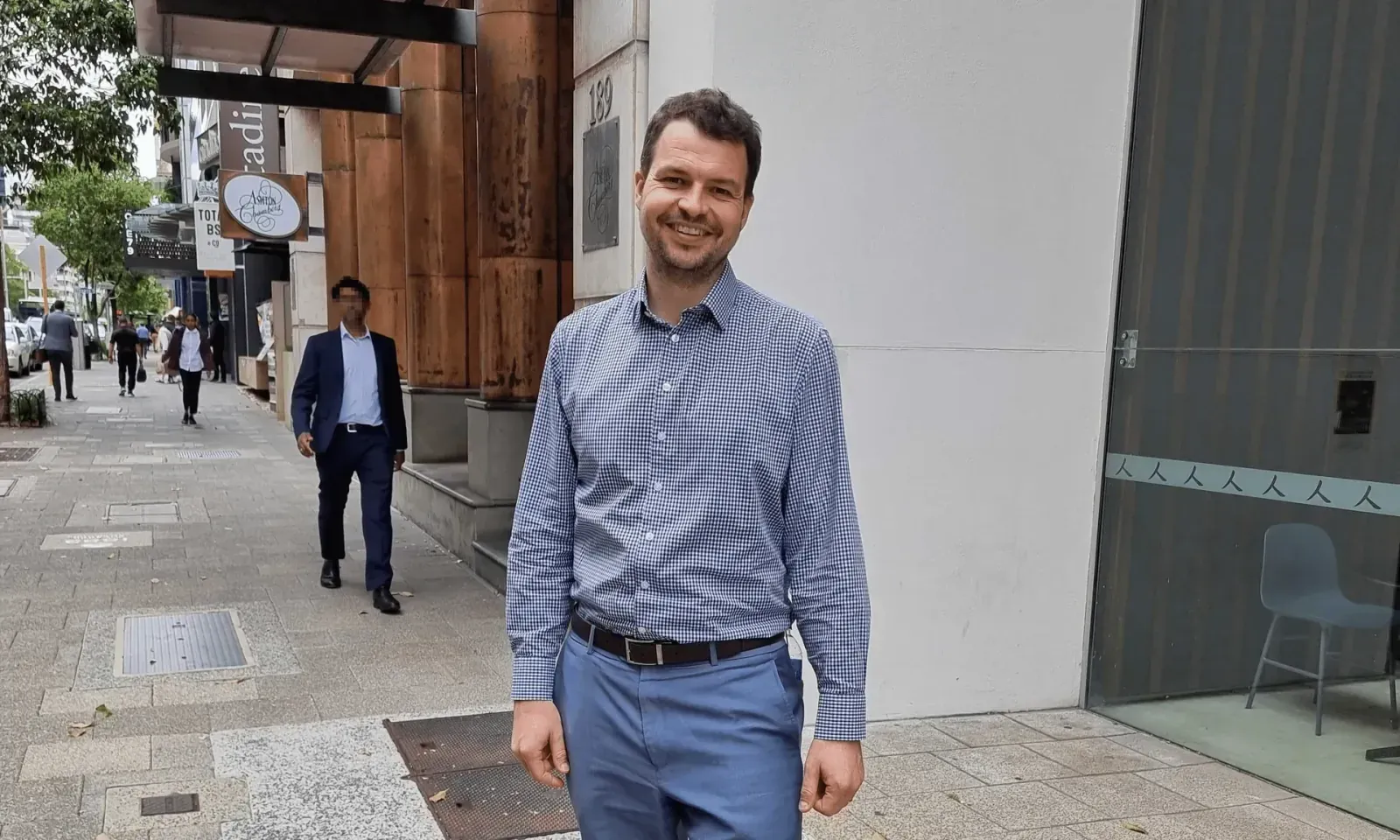 Adam Mullett, product roadmap author, smiling in a blue checked shirt on a city sidewalk