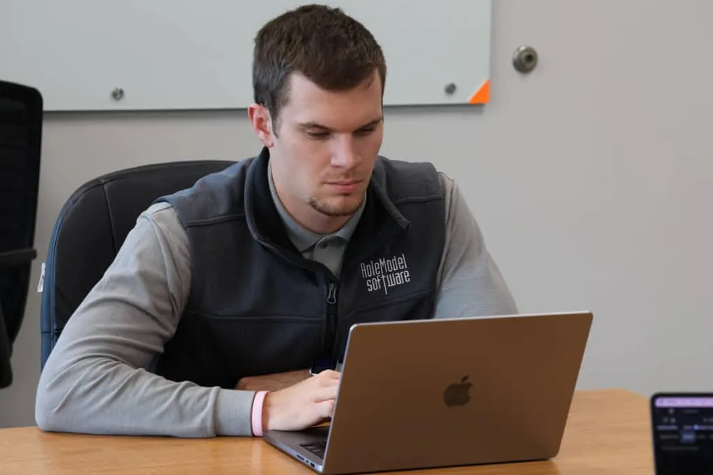 RoleModel Software team member in a branded vest working on a laptop at a meeting room table