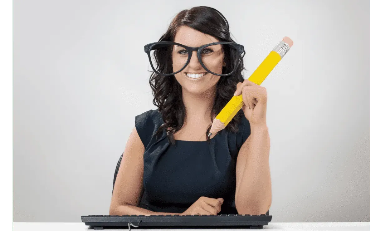 Smiling woman in oversized novelty glasses holding a giant yellow pencil at a keyboard